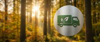 Green delivery truck icon with leaf symbol on metallic circle badge against golden autumn forest background with sunlight rays filtering through trees.
