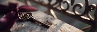 Vintage brass key lying on aged paper with burgundy ribbon, creating nostalgic atmosphere in soft natural lighting, dramatic panoramic composition.