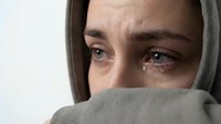 Young woman with tears in eyes covered by gray fabric showing emotional distress and sadness in close-up portrait for mental health awareness campaigns.
