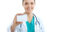 Young female healthcare professional with Caucasian ethnicity wearing white medical coat and teal scrubs, holding blank business card or ID badge. Stethoscope visible around neck. Suitable for medical, healthcare, hospital, clinic, and professional services marketing materials.