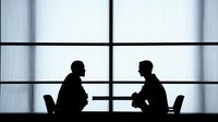 Two business professionals in silhouette having discussion at modern office window, corporate meeting concept for presentations and workplace communication.