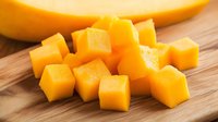 Fresh ripe mango cut into uniform cubes on wooden cutting board, bright yellow-orange tropical fruit pieces ready for healthy eating and food design.