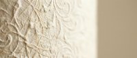 Textured cream wall surface with intricate raised floral pattern casting soft shadows in natural light for interior design and architectural backgrounds.