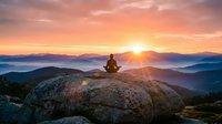 Person meditating on mountain rock at sunrise with layered peaks and golden sky. Peaceful wellness concept for mindfulness and spiritual practice.