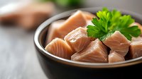 Fresh raw salmon cubes in black ceramic bowl with parsley garnish on wooden table, selective focus. Healthy omega-3 rich seafood for cooking.