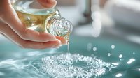 Woman pouring essential oil from glass bottle into water with bubbles, creating aromatic spa treatment for skincare and relaxation.