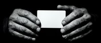 Elderly hands holding blank white business card against dark background in monochrome style for professional presentation and corporate identity design.