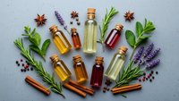 Essential oils in glass bottles with cork stoppers surrounded by fresh herbs, spices and lavender sprigs on gray background for aromatherapy and wellness.