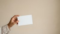 Cropped view of a woman's hand holding a blank white card against a neutral beige background, suitable for business card mockups and promotional designs.