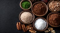 Assorted superfood powders and nuts in wooden bowls on dark slate background for healthy cooking and nutrition supplements.