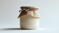 Glass jar with natural yogurt or milk product covered with burlap fabric and twine on white background, minimalist food photography style.