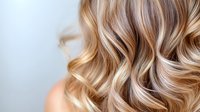 Close up of wavy blonde highlighted hair with soft balayage technique showing natural movement and texture against light background, modern hairstyling concept.