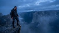 Middle-aged Caucasian male hiker standing on dramatic cliff edge overlooking misty canyon during blue hour twilight for adventure travel concepts.