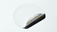 White round adhesive sticker with curled corner edge peeling up showing black backing, isolated on white background for graphic design projects.