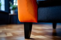 Modern orange and navy blue armchair leg detail on wooden floor, shallow depth of field creates artistic interior design composition with soft bokeh effect.
