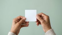 Hands of a middle-aged man with medium skin tone holding a blank white card against a soft sage green background, suitable for mockups, branding, and promotional materials.