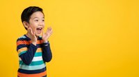 Young Asian boy, approximately 4-6 years old, wearing colorful striped long-sleeve shirt, shouting or calling out with hands near mouth against bright yellow background.