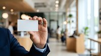Businessman in dark suit holding blank white business card in modern office lobby with blurred background, networking and corporate identity concept.