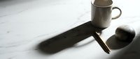 White ceramic coffee mug casting dramatic shadow on marble surface with spoon, minimalist morning beverage concept for kitchen and lifestyle design.