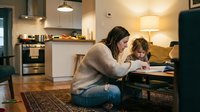 Mother helping young child with homework at kitchen table in modern home interior with warm lighting and cozy atmosphere for family education concepts.