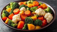 Fresh mixed vegetables including broccoli, cauliflower, carrots and bell peppers arranged in rustic bowl on dark slate background for healthy cooking.