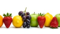 Fresh colorful fruits in a row on white background, including strawberries, grapes, green apples, and lemons, healthy eating concept.