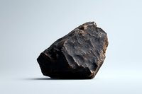 Raw black meteorite fragment with rough textured surface and dark crystalline structure against neutral background, showcasing natural cosmic material formation.