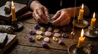 Fortune teller hands reading crystals and gemstones on wooden table with candles for spiritual guidance and divination practices.