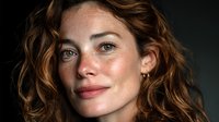 Professional portrait of confident Caucasian woman with wavy brown hair and natural freckles against dark background for business and lifestyle content.