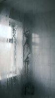 Water droplets and condensation on glass shower door creating abstract patterns with blurred bathroom background for spa and wellness concepts.