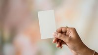 Close-up of hand holding blank white card against blurred background, suitable for business cards, invitations, marketing materials, and promotional designs.