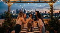 Four young women celebrating with champagne glasses on rooftop terrace at sunset with city skyline and string lights creating festive atmosphere.