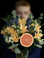 Fresh spring bouquet with orange lilies, purple muscari and grapefruit slice held by young woman on dark background for seasonal floral design concepts.