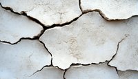 Cracked white wall surface with deep fissures showing structural damage and weathering effects. Natural pattern of breaks creates abstract geometric shapes.