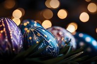 Festive blue and purple glass ornaments with glitter patterns against blurred golden bokeh lights and evergreen branches create magical holiday atmosphere.