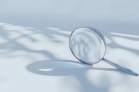 Magnifying glass on white surface with soft shadow patterns, symbolizing search, investigation, and discovery in business or science.