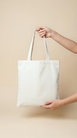 Female hands holding blank white cotton tote bag mockup on beige background for branding and design customization.
