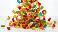 Colorful assorted gummy candies pile with bears, rings, worms in red, green, yellow, orange colors on white background for sweet treats and confectionery designs.