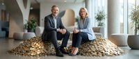 Successful mature business partners sitting on pile of golden coins in modern office lobby discussing financial growth and investment strategies.