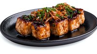 Grilled tofu steaks with teriyaki glaze and fresh herbs on black plate. Plant-based protein meal for healthy dining and vegetarian cuisine photography.
