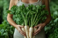 Fresh organic parsnips with green leaves held by woman in linen apron against garden background, farm to table produce for healthy cooking and nutrition.