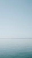 Serene seascape with calm turquoise waters meeting a misty horizon, featuring minimalist composition with soft gradient sky transitioning from pale blue to white tones.