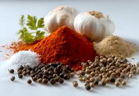 Fresh garlic bulbs with heaps of vibrant paprika, salt, coriander seeds, black peppercorns, and ground spices on white background for cooking and seasoning dishes.