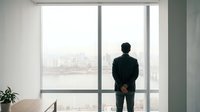 Professional businessman in dark suit standing at large office window overlooking city skyline, contemplating future business opportunities and success.