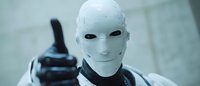 Futuristic android with white face mask showing thumbs up gesture against blurred background, representing artificial intelligence and robotics advancement.