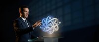 Young professional businessman in dark suit presenting glowing digital brain with gears hologram, representing artificial intelligence and innovation concepts.