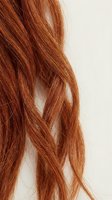 Close-up of flowing auburn red hair strands with natural texture and shine against neutral background for beauty and haircare concepts.