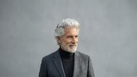 Mature man with white hair and beard wearing gray blazer and black turtleneck against neutral background. Suitable for business, corporate, lifestyle, and professional portraits.