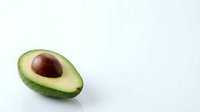Fresh ripe avocado half with pit on white background isolated for healthy cooking and nutrition design projects.
