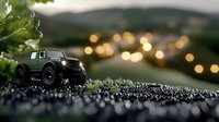 Green off-road toy vehicle on wet ground with bokeh lights in background creates dreamy outdoor adventure scene with shallow depth of field effect.